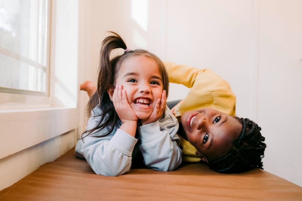 Two little girls who look different from each other laugh and play as foster siblings.