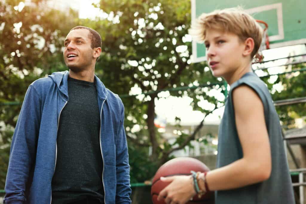 A man plays basketball with with a young man that he mentors.