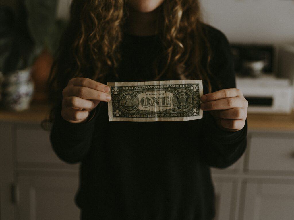 A teen aging out of foster care holds up a dollar bill to show she's planning for a strong financial future.