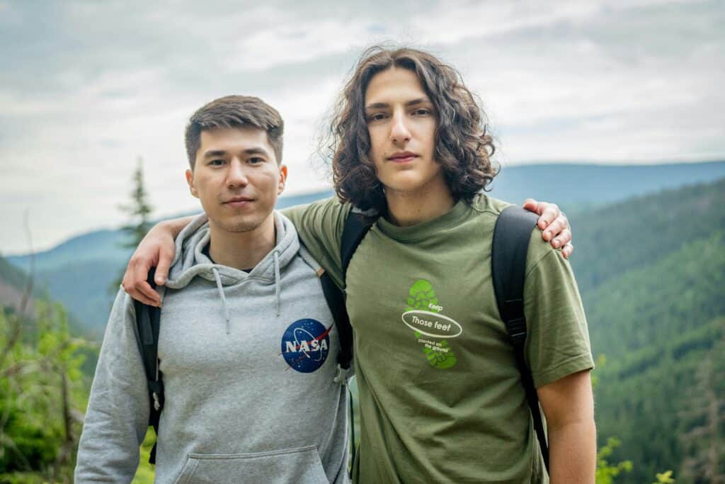 Two young men aging out of foster care stand side-by-side on top of a mountain they just hiked together.
